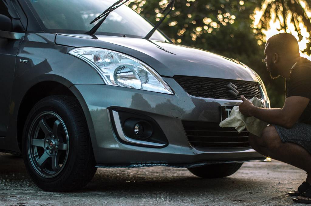 A man cleaning the front of his car with a wipe.