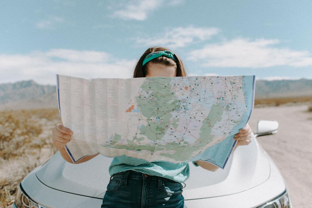 A person looking at a map while leaning on their car hood.