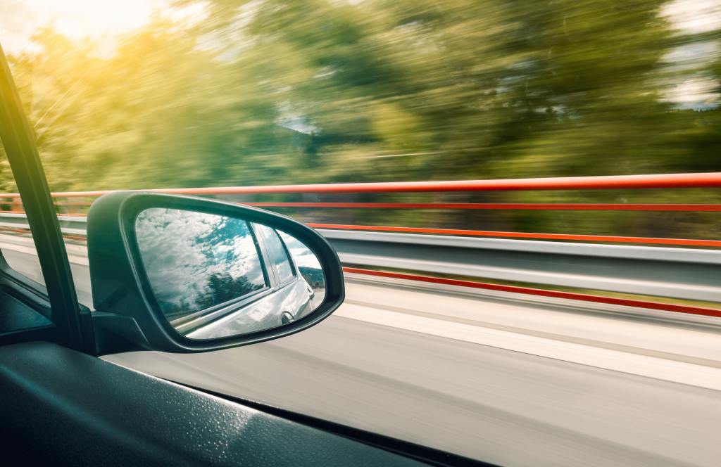 A view of a car's side mirror while speeding down a highway.